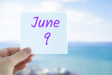 June 9th. Hand holding sticker with text June 9 on the blurred background of the sea and sky. Copy space for text. Month in calendar concept