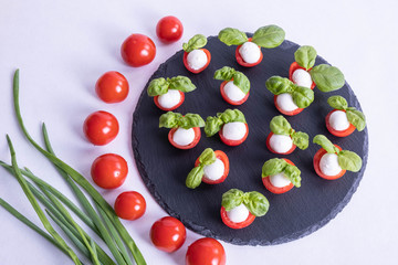 green onions and a composition of basil, tomatoes, mozzarella on a stone black tile