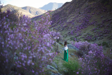 A girl walks in bloom of flowers against the backdrop of a mountain landscape.