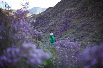 A girl walks in bloom of flowers against the backdrop of a mountain landscape.