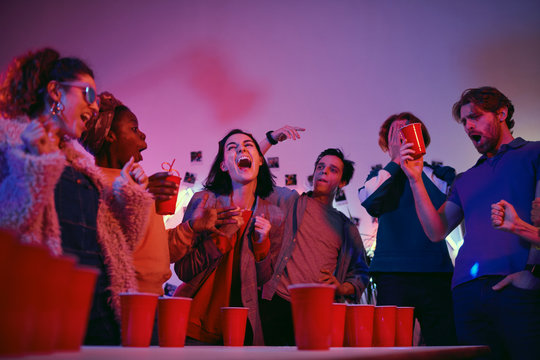 Young woman laughing while playing in beer pong game together with her friends during a party