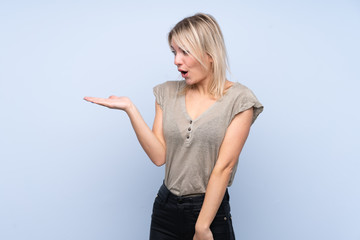 Young blonde woman over isolated blue background holding copyspace imaginary on the palm