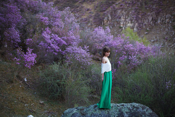 A girl walks in bloom of flowers against the backdrop of a mountain landscape.