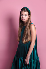 Fashion beautiful young girl in satin emerald dress with long hair posing in studio.