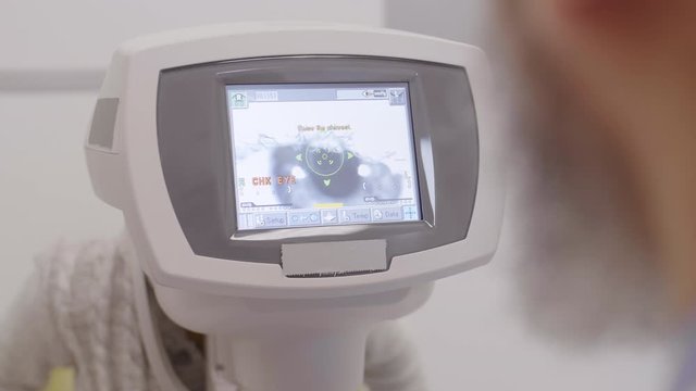 Over the shoulder shot of professional optometrist looking at autorefractor screen displaying eye of little boy during vision test in ophthalmology clinic