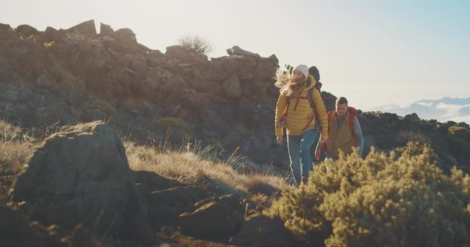 Young adventurous backpacking couple hiking up a rocky mountain at sunset above the clouds