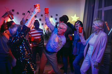 Senior man drinking beer and having fun with young people during party at home