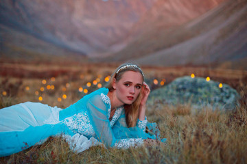 A girl in a blue dress walks in the evening against the backdrop of mountains in the light of...