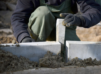 A worker puts a concrete wedge between two concrete curbs.