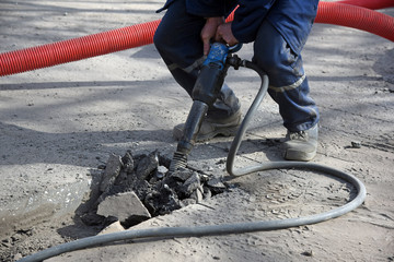 A worker breaks the asphalt with a jackhammer, repairing a motorway road.