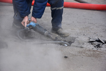 A worker breaks the asphalt with a jackhammer, a lot of dust.