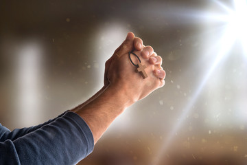 Obraz na płótnie Canvas Man praying in church with closed hands and cross flash