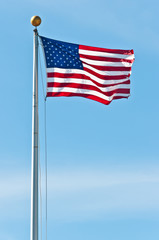 Front view, far distance of the american flag, fluttering in the breeze on a tall aluminum pole with a blue sky