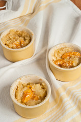 Top view, close distance of three yellow, ceramic cups filled with freshly baked, homemade, Apricot Sour Cream Crumble-on white table cloth
