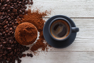 Grey cup of coffee with foam, roasted and ground beans on wooden table. Closeup, copy space, top view. Coffee shop, espresso, fresh roast, drink  concept