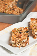 top, front view of two freshly baked, homemade, Granola Bars, on a white, yellow tea towel with a metal baking pan filled with 