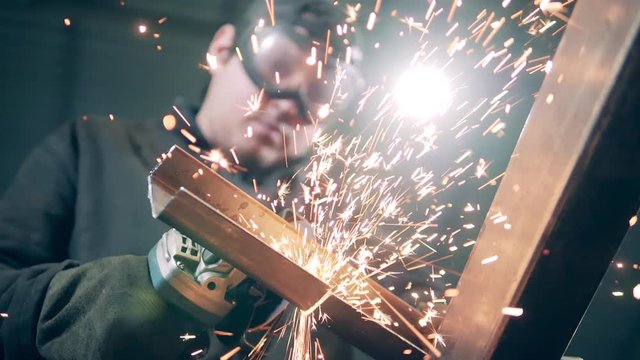 Male worker uses angle grinder at a plant.