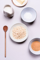 Ingredients for oat porridge: rolled oats or flakes, sugar, salt, milk and butter in a bowls on grey concrete background. Healthy eating, vegetarian food concept. Top view. Selective focus