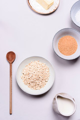 Ingredients for oat porridge: rolled oats or flakes, sugar, salt, milk and butter in a bowls on grey concrete background. Healthy eating, vegetarian food concept. Top view. Selective focus