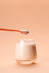 Coconut or almond milk with collagen spoon on pastel coral background