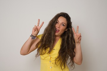 Isolated shot of cheerful woman makes peace or victory sign with both hands, dressed in casual clothes, feels cool has toothy smile, isolated over gray background. People and body language.