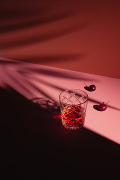 Red Cherry Cocktail with Fresh Cherries on Pink Background with Plant Shadows