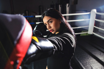 A beautiful girl in boxing gloves hits her paws in the ring. Sexy woman is training in the gym....