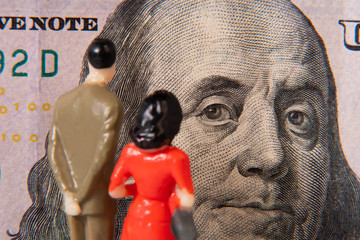 Male and female miniature figures examining a US 100 dollar bill