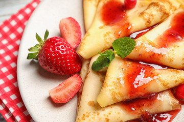 Delicious thin pancakes with strawberries and jam on plate, closeup