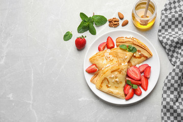 Delicious thin pancakes with strawberries, cottage cheese and honey on light table, flat lay. Space...