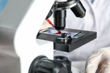 Scientist dripping blood sample onto slide on microscope in laboratory, closeup. Virus research