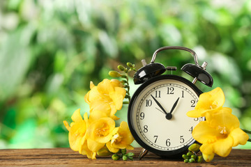 Alarm clock and beautiful spring flowers on wooden table. Time change concept