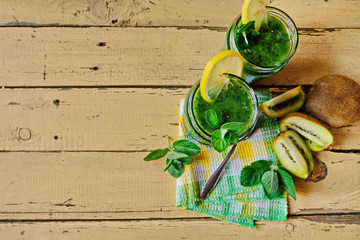 Green homemade cocktails in two glass jars on a wooden table on a checkered napkin. Ingredients-lemon, spinach, kiwi, mint. Copy space. Top view