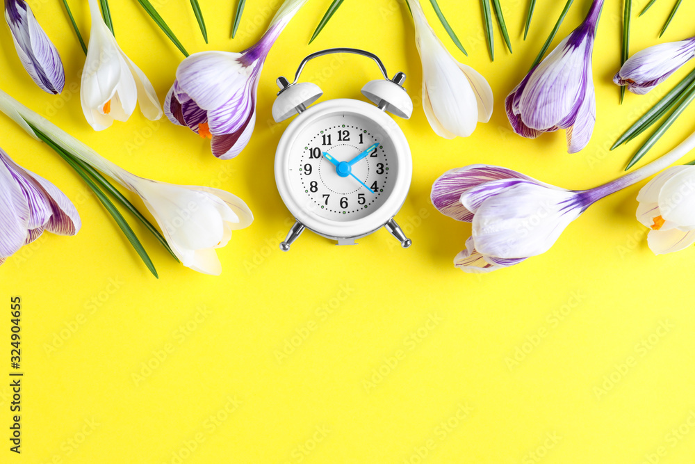 Poster white alarm clock with spring flowers and space for text on yellow background, flat lay. time change