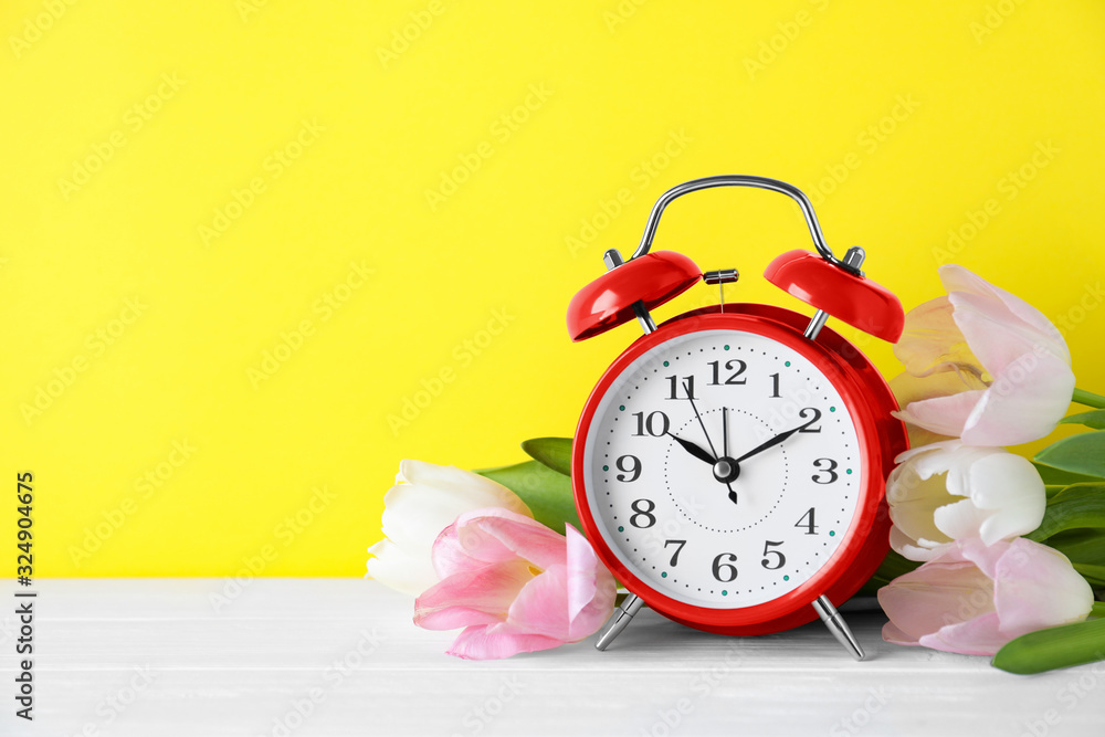 Poster red alarm clock and spring flowers on yellow background, space for text. time change