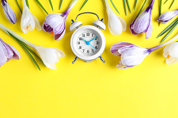 White alarm clock with spring flowers and space for text on yellow background, flat lay. Time change
