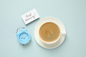 Delicious coffee, alarm clock and card with GOOD MORNING wish on light background, flat lay