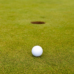 Golf ball on green over a blurred hole. Shallow depth of field. Focus on the ball.