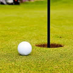 Golf ball on green with flag. Shallow depth of field. Focus on the ball.