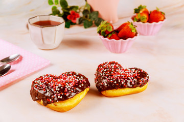 Two heart shaped donuts with chocolate glaze and pink, red sprinkles on a platet with strawberry.