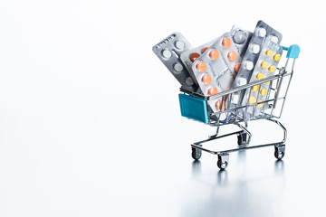 A set of medicines in a shopping trolley. Pills in a blister, antibiotics in glass bottles, ampoules for injection on a white background.