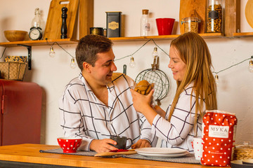 A couple in love of European nationality. With smiling, happy faces, they prepare Breakfast in the kitchen, in pajamas. Hold cookies in your hands. Horizontal photo.