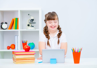 Girl with down syndrome is engaged with a tablet computer at home, smiles while looking at the...
