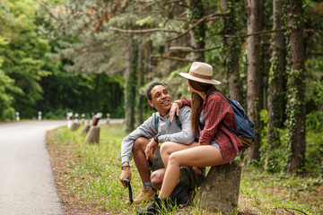 Two  friends hiking in nature.They sitting and resting by the old country road.	
