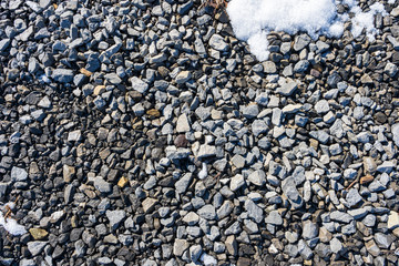 Dirty grey stones of varying sizes lay in the sunshine on a gravel driveway.