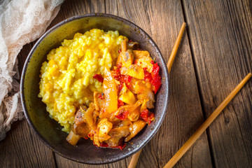 Saffron rice with pieces of chicken and vegetables on wooden table.