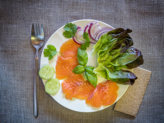 Close-up  top view on thinly slices of smoked salmon on fish fork and on white dish and gray linen...