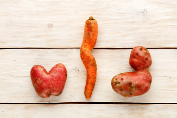 Ugly potato in the heart shape and twisted carrot on a white wooden background. Vegetable or food...