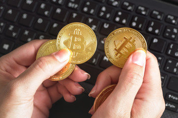 Woman hand holding golden coloured bitcoin coin over black laptop keyboard