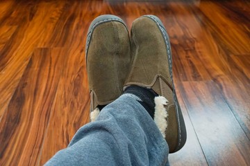 A man Crossing his legs and wearing brown household slippers